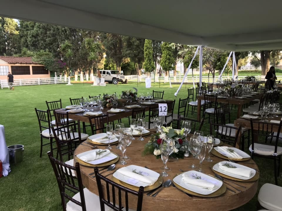 Montaje de banquete con mesas redondas y sillas Chiavari bajo carpa para boda en el jardín de Rancho San Antonio