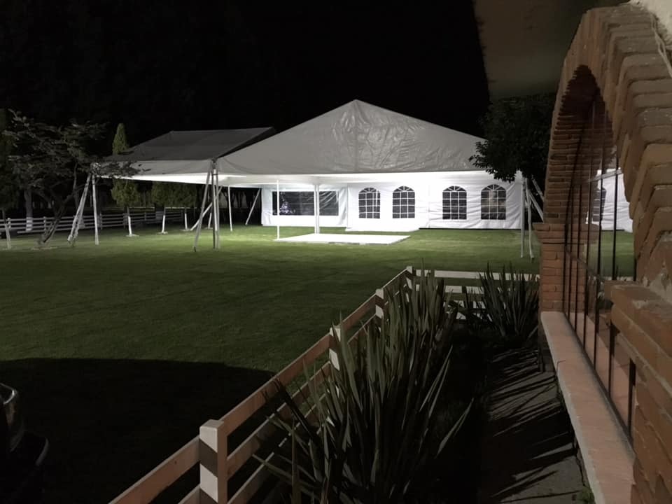 Carpa iluminada de noche con vista exterior desde el jardín, ideal para bodas nocturnas en Rancho San Antonio