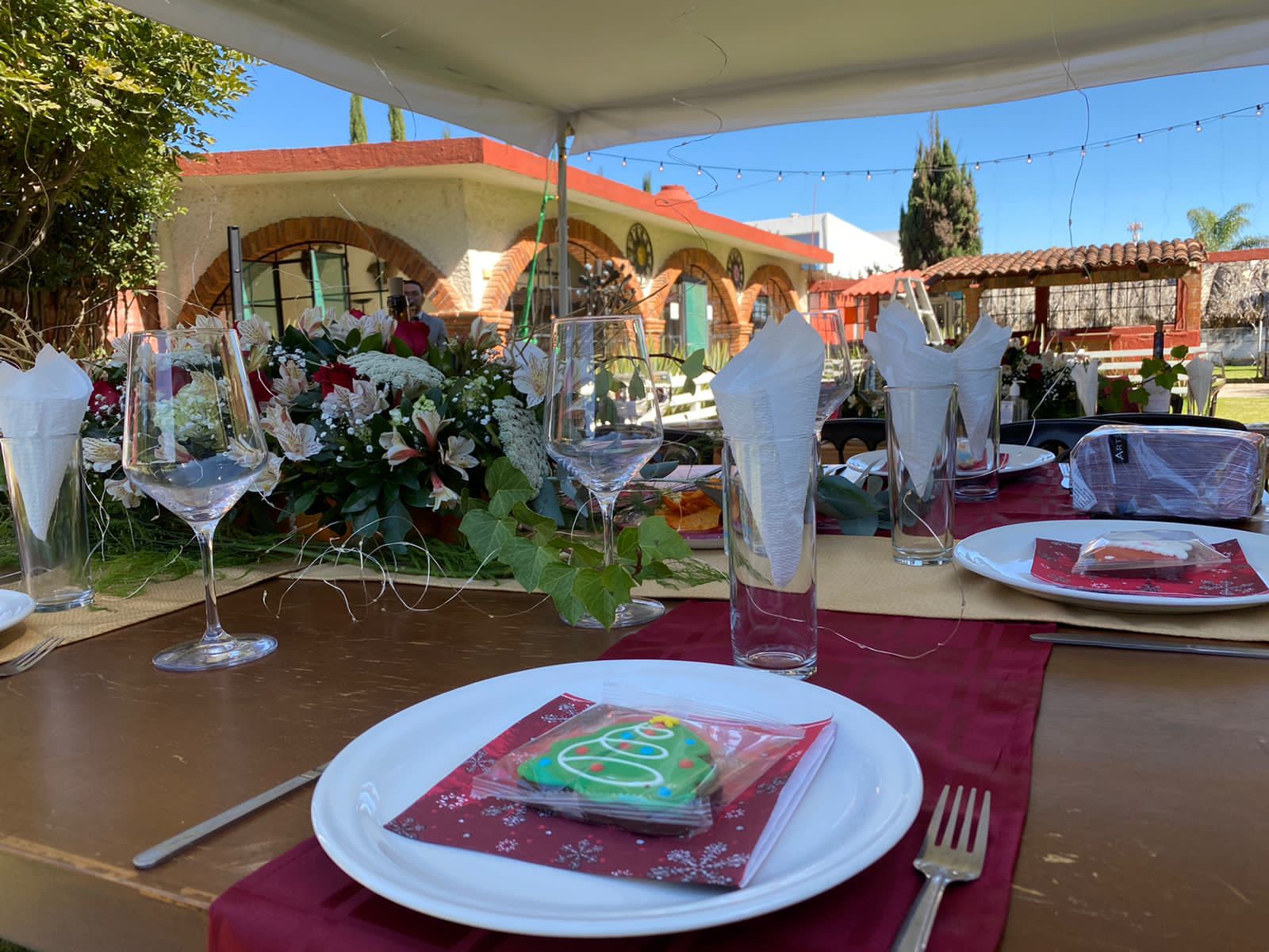 Mesa navideña con arreglos florales y galleta decorativa frente a la fachada con arcos de ladrillo del rancho
